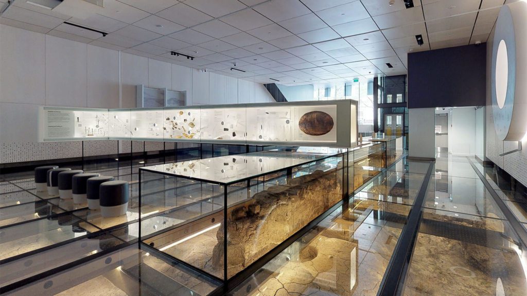 Inside a modern museum in Montreal, featuring an innovative exhibit design with glass floors showcasing archaeological artifacts. The space is illuminated by ambient lighting, highlighting informational displays and minimalist seating areas. This museum offers a blend of history and contemporary design, appealing to visitors interested in both heritage and modern architecture.
