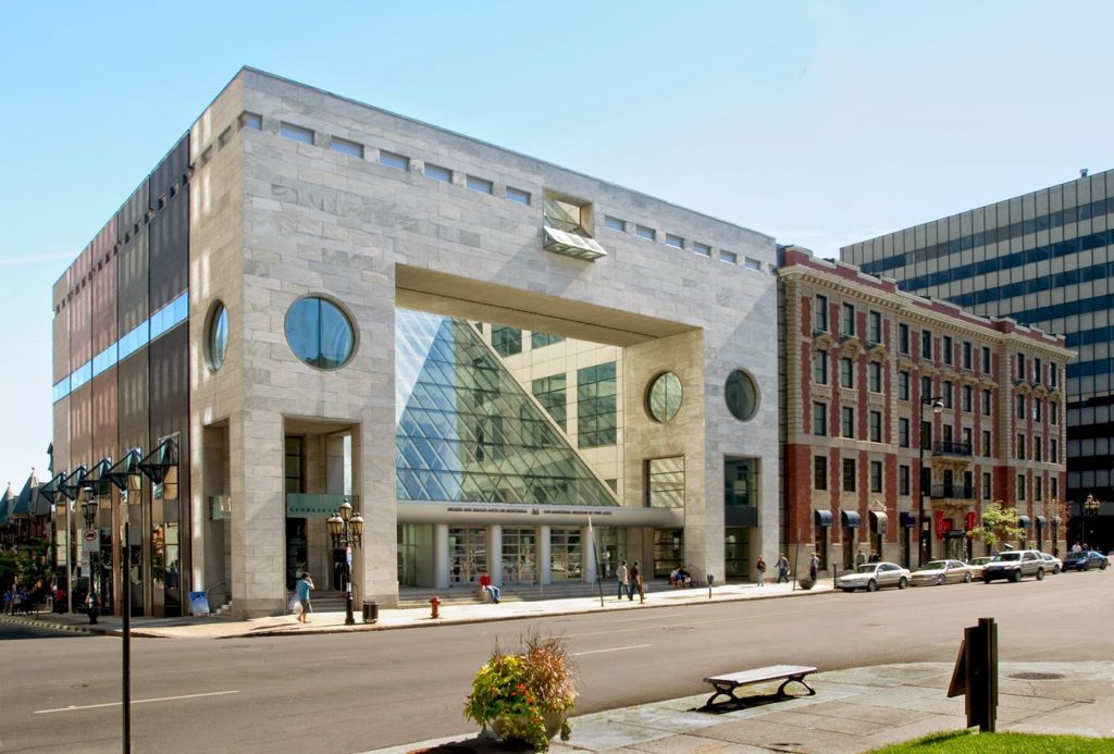 The modern facade of the Montreal Museum of Contemporary Art, featuring a unique architectural design with large circular windows and angular glass sections. Located in a vibrant urban area, the museum contrasts with the traditional brick buildings nearby, highlighting Montreal's blend of historic and contemporary styles.