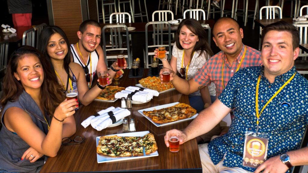 A diverse group enjoying craft beers and artisan pizzas at a local brewery, during a food and drink tour with City Brew Tours.