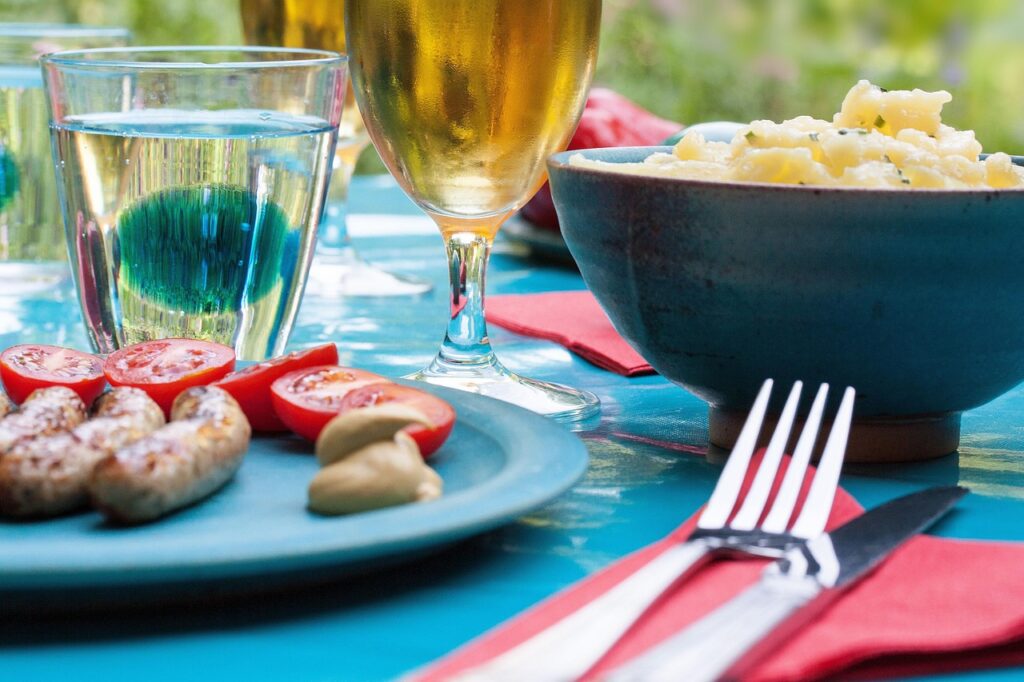Delicious outdoor meal with sausages, tomatoes, mustard, and a refreshing drink, perfect for a casual bachelorette party gathering