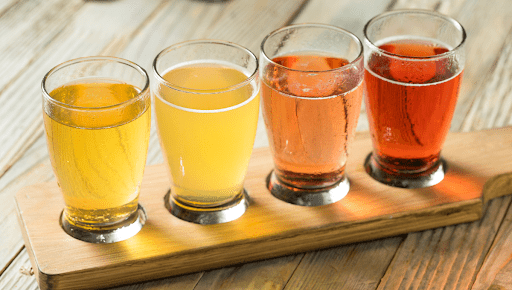 Colorful flight of different beer styles including amber ale, wheat beer, and sour beer served on a wooden board for tasting.