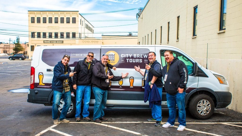 A group of tour guests pose in front of the Pittsburgh Brew Tour van.
