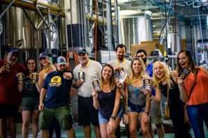 A large City Brew Tours group poses for a photo in the production facility of a local craft brewery.